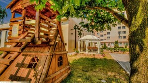 A wooden playhouse with a sign, a gazebo, and a building in the background. - Confero (Nysa)