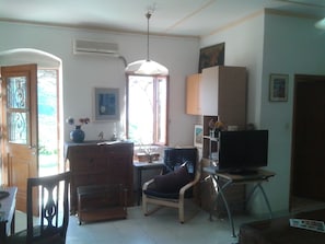 Un salon avec un meuble en bois, un téléviseur posé sur un meuble, une chaise et un bureau avec une lampe.