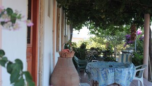 Une terrasse extérieure avec une table et des chaises, un grand vase et un panier posé sur la table.