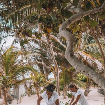 A massage therapy session on a beach with palm trees and a sandy environment.