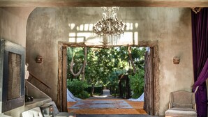A room with a large window, a chandelier, and a view of a garden. - Casa Malca (Tulum)