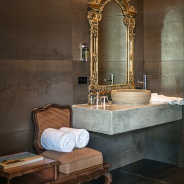A bathroom with a marble vanity, a large ornate mirror, and a wooden chair with towels.