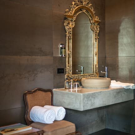 A bathroom with a marble vanity, a large ornate mirror, and a wooden chair with towels.