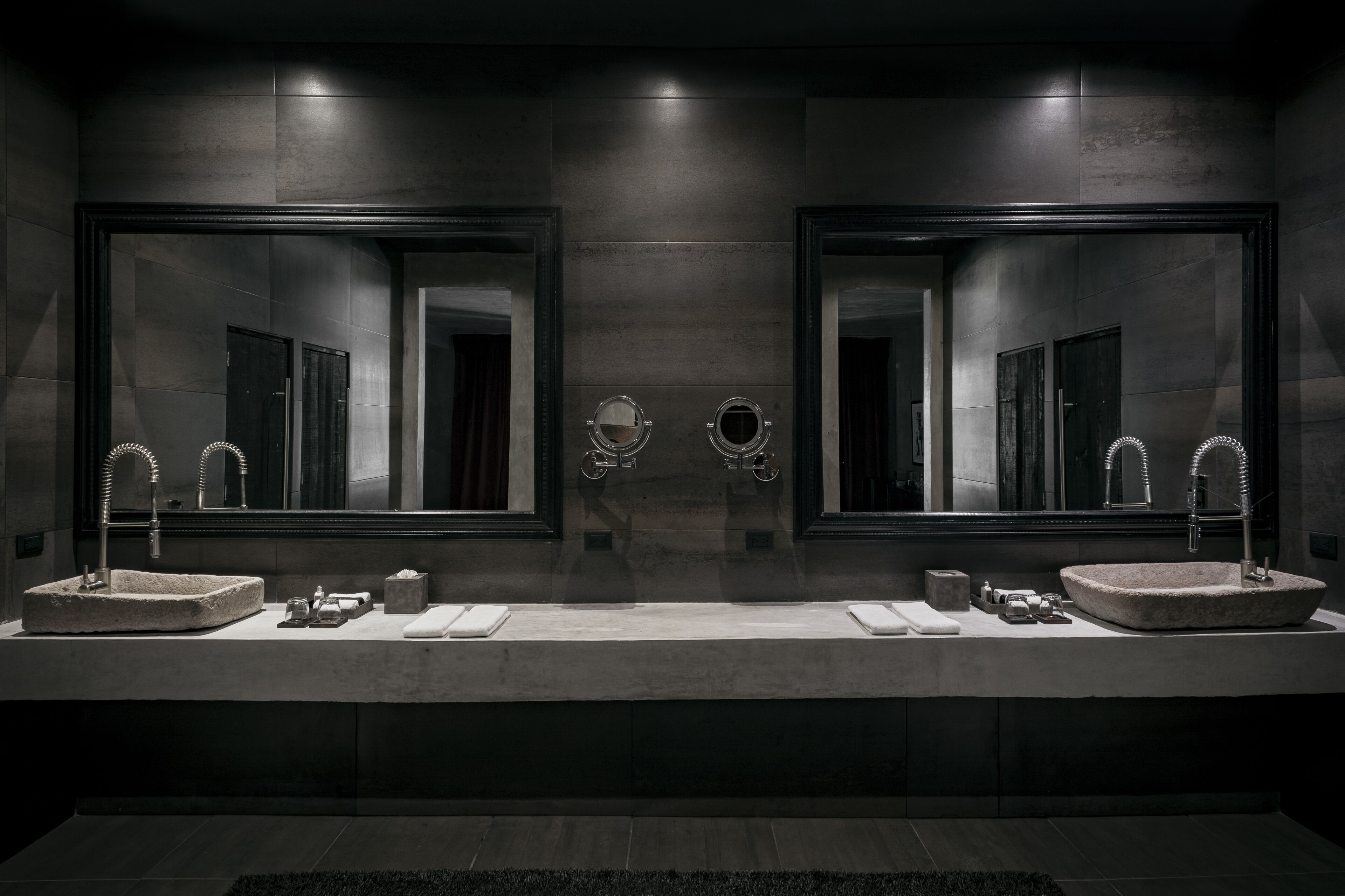 Ein modernes Badezimmer mit zwei großen Spiegeln, einem runden Spiegel in der Mitte und zwei Waschbecken mit Wasserhähnen.
