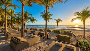 Un espace de détente aménagé sur la plage, avec des chaises longues et des palmiers, offrant une vue sur l’océan.