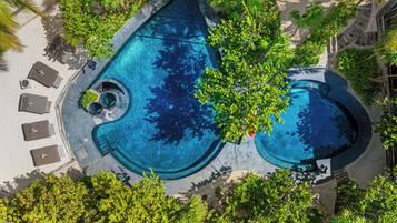 An aerial view of a swimming pool surrounded by lush greenery and shaded by palm trees.