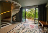 A modern interior with a spiral staircase, a large window with a view of greenery, and a patterned rug.