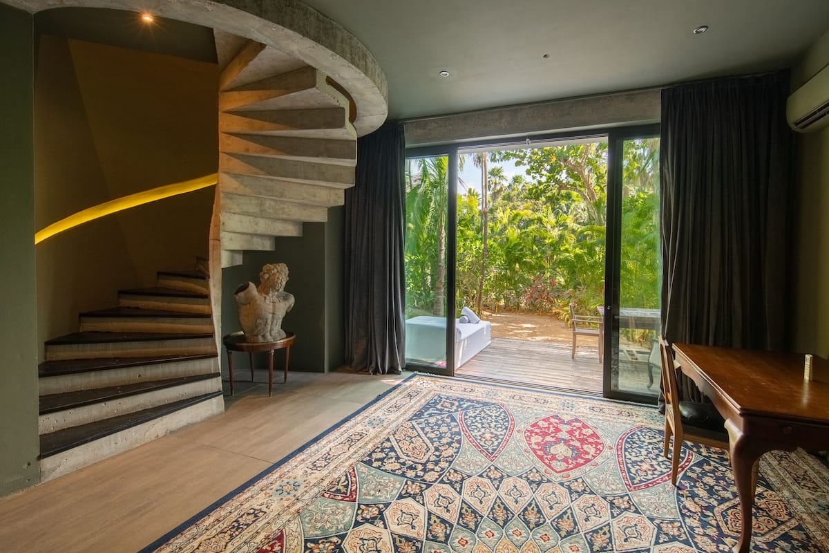 Un intérieur moderne avec un escalier en colimaçon, une grande fenêtre donnant sur un paysage verdoyant et un tapis à motifs.