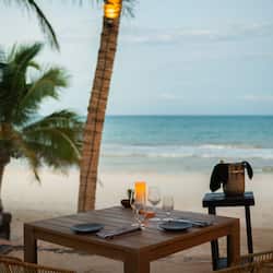 Enjoy a romantic beachside dinner for two, with a table set amidst palm trees and a serene ocean view.