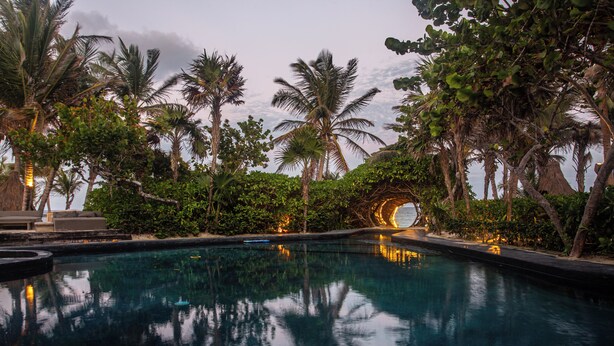 A serene pool area with palm trees and a circular stone structure. - Casa Malca (Tulum)
