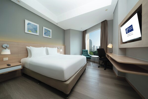 Une chambre d’hôtel avec un lit, un bureau, une chaise, une télévision et une vue sur la ville.