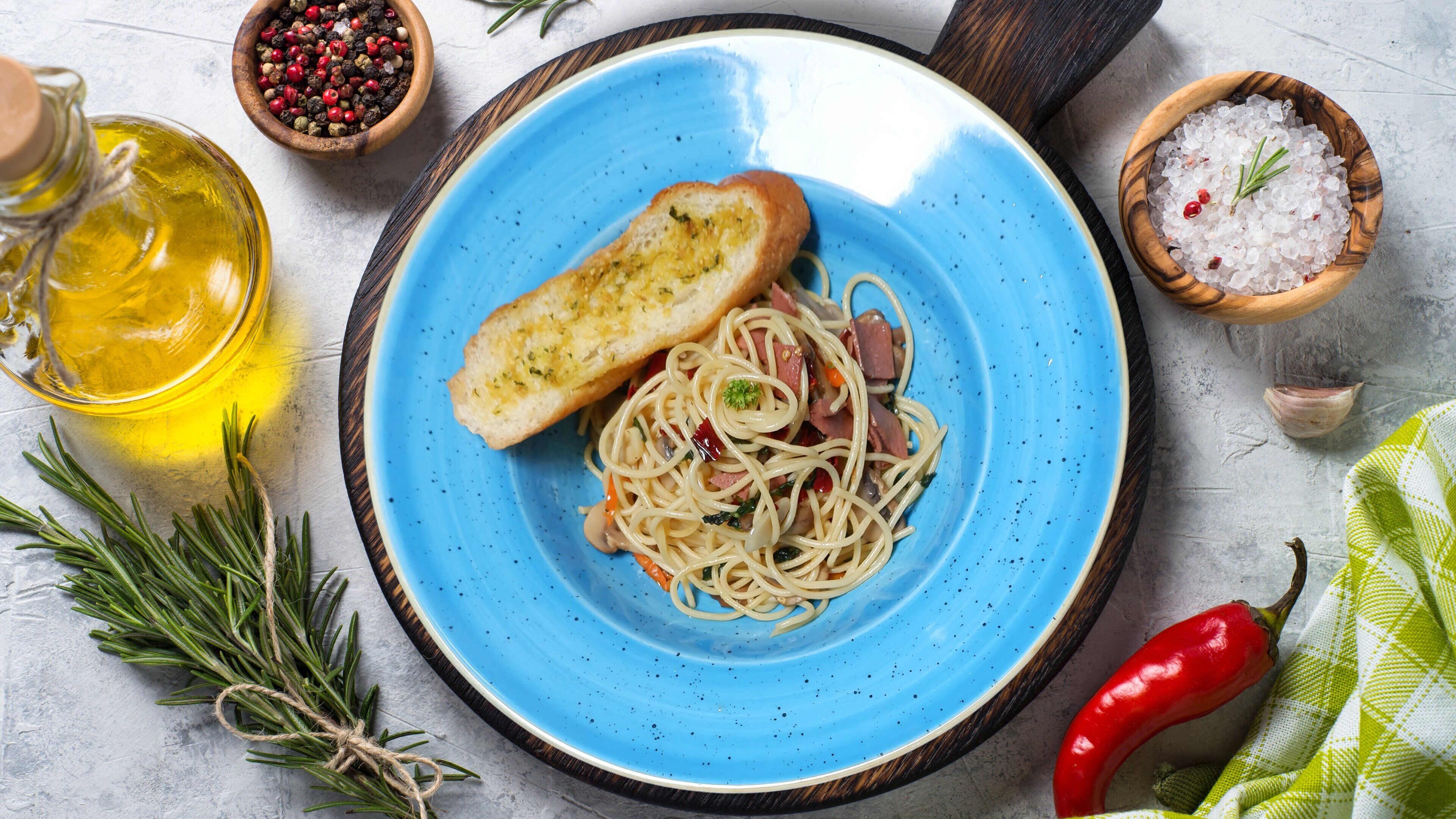 A plate of spaghetti with meat and herbs, a bottle of olive oil, and a bowl of peppercorns.