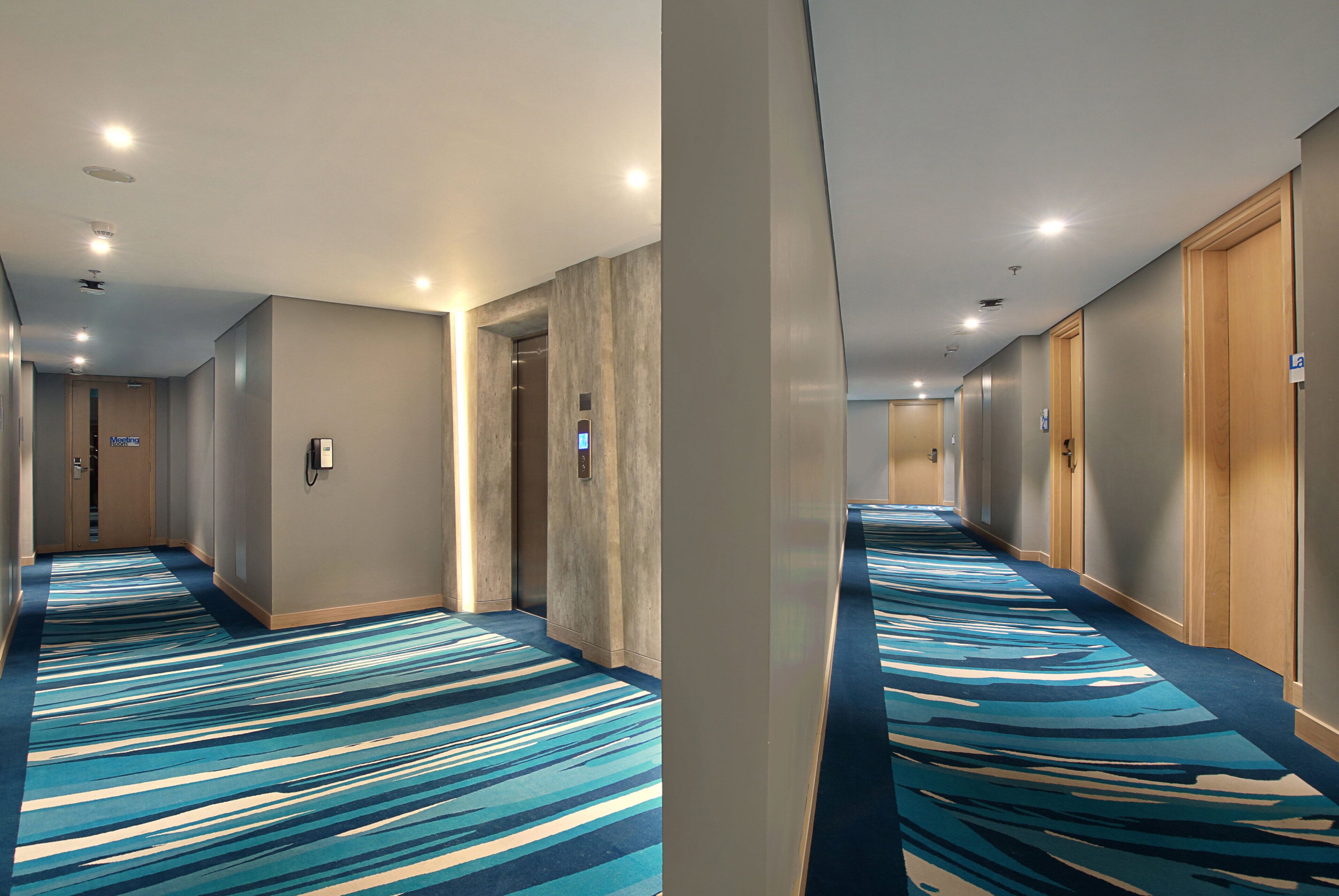 A hotel hallway with carpeted floors, wooden doors, and a meeting room sign.