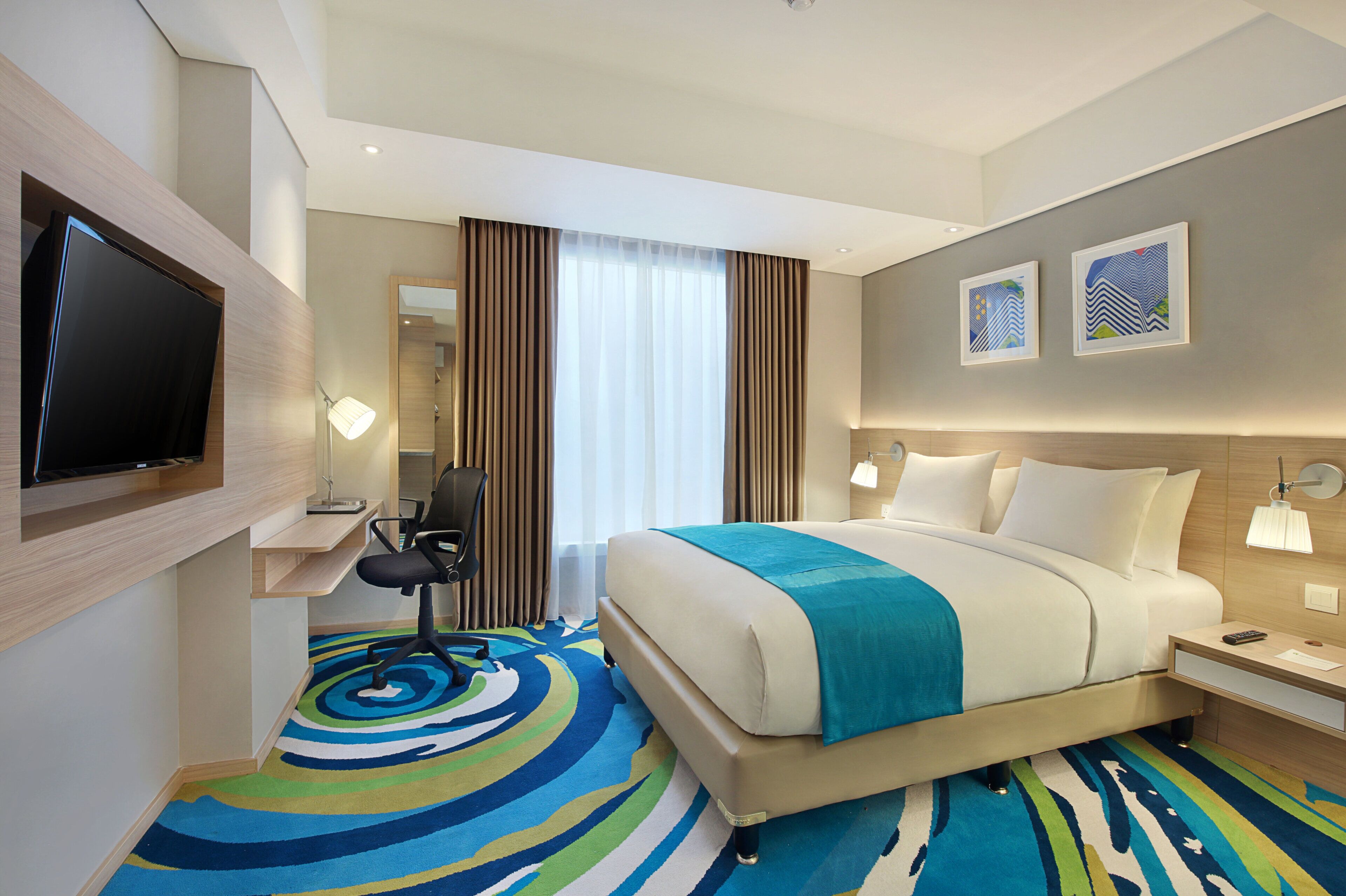 Una habitación de hotel con cama, escritorio, silla, televisor y obras de arte en la pared.