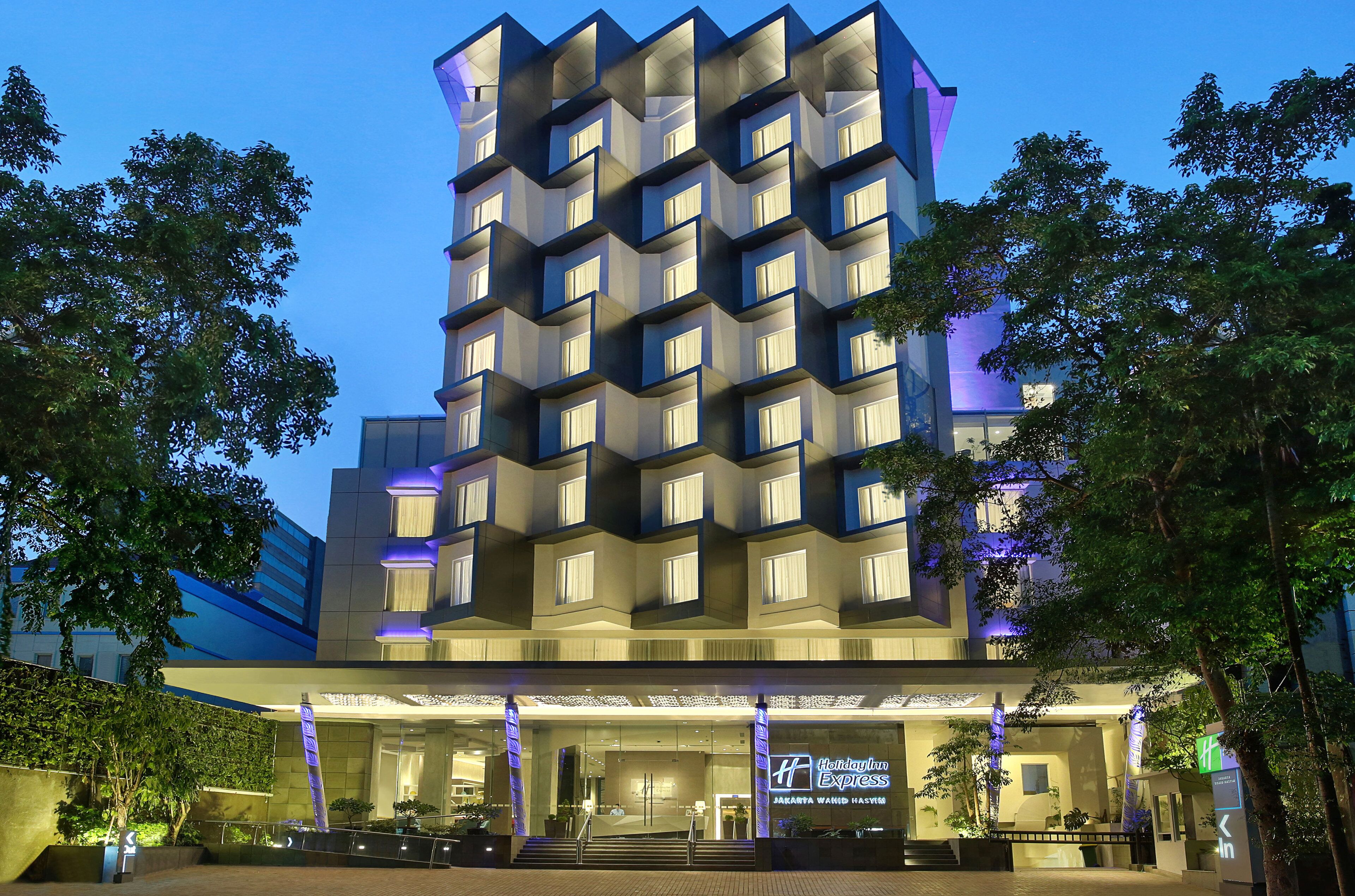 A modern hotel with a unique geometric facade, multiple balconies, and a well-lit entrance.