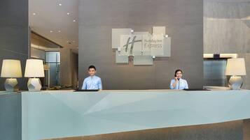 A hotel reception desk with two staff members, a modern interior design, and a visible elevator.