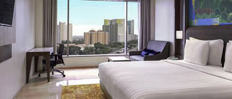 Una habitación de hotel con una cama grande, un escritorio, una silla y vistas a edificios de la ciudad.