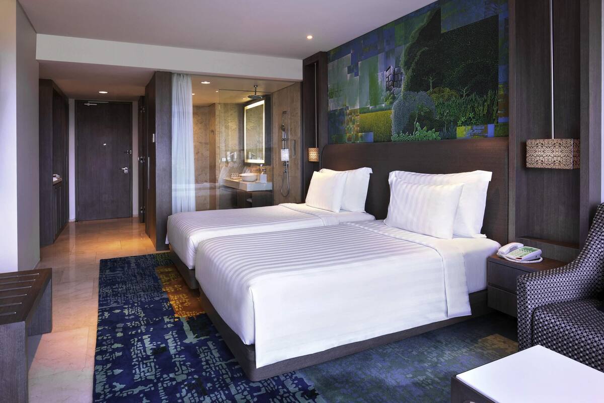 A hotel room with a large bed, a bathroom with a mirror, a nightstand, and a wall-mounted telephone.