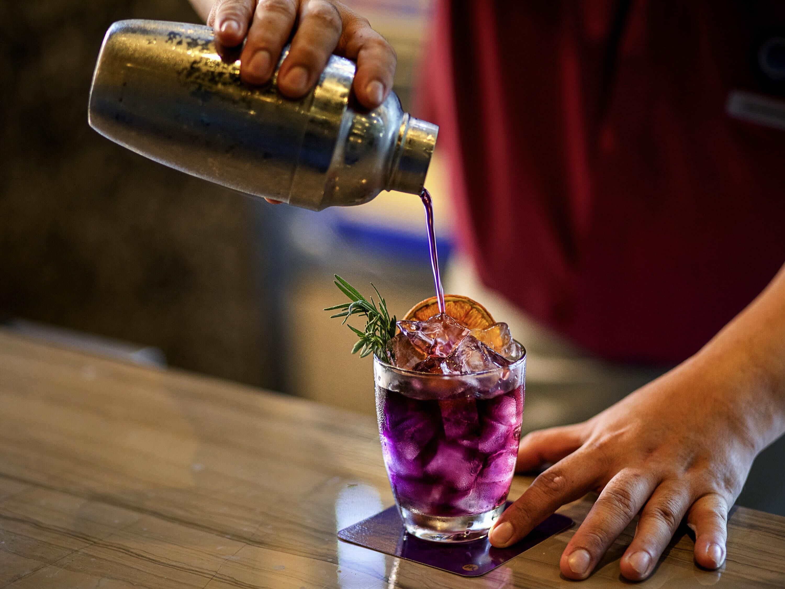 A bartender pouring a drink into a glass with ice and a garnish.