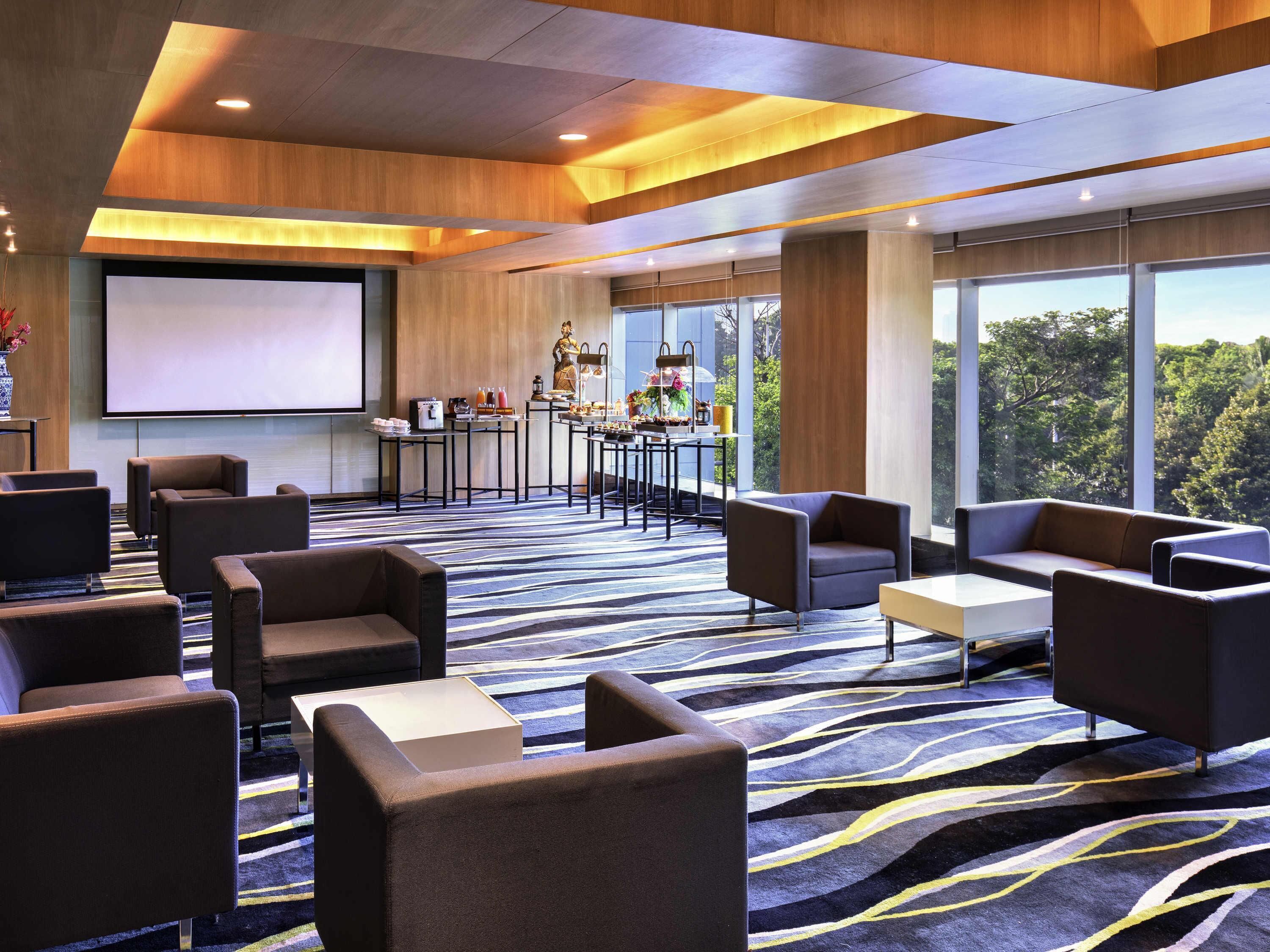 A modern hotel lobby with a large screen, comfortable seating, a bar area, and large windows offering a view of the outdoors.