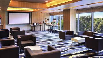 A modern hotel lobby with a large screen, comfortable seating, a bar area, and large windows offering a view of the outdoors.