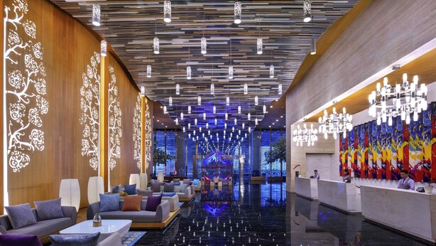 A modern lobby with a reflective black floor, seating areas with sofas and armchairs, a reception desk, and a colorful abstract mural on the right wall. - Grand Mercure Jakarta Kemayoran (Jakarta)