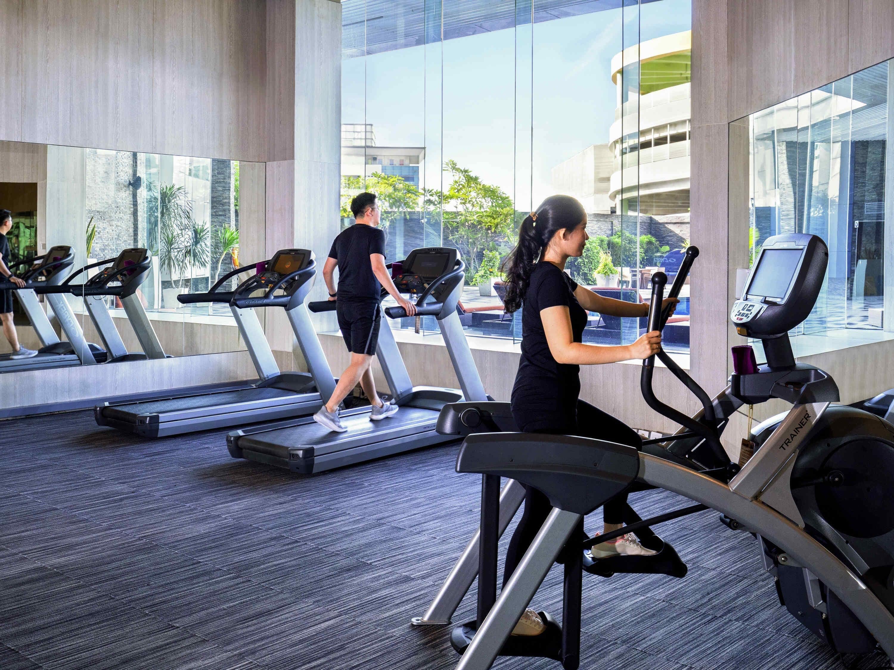 Un gimnasio con cintas de correr, una bicicleta estática y un ventanal con vistas a edificios y zonas verdes.