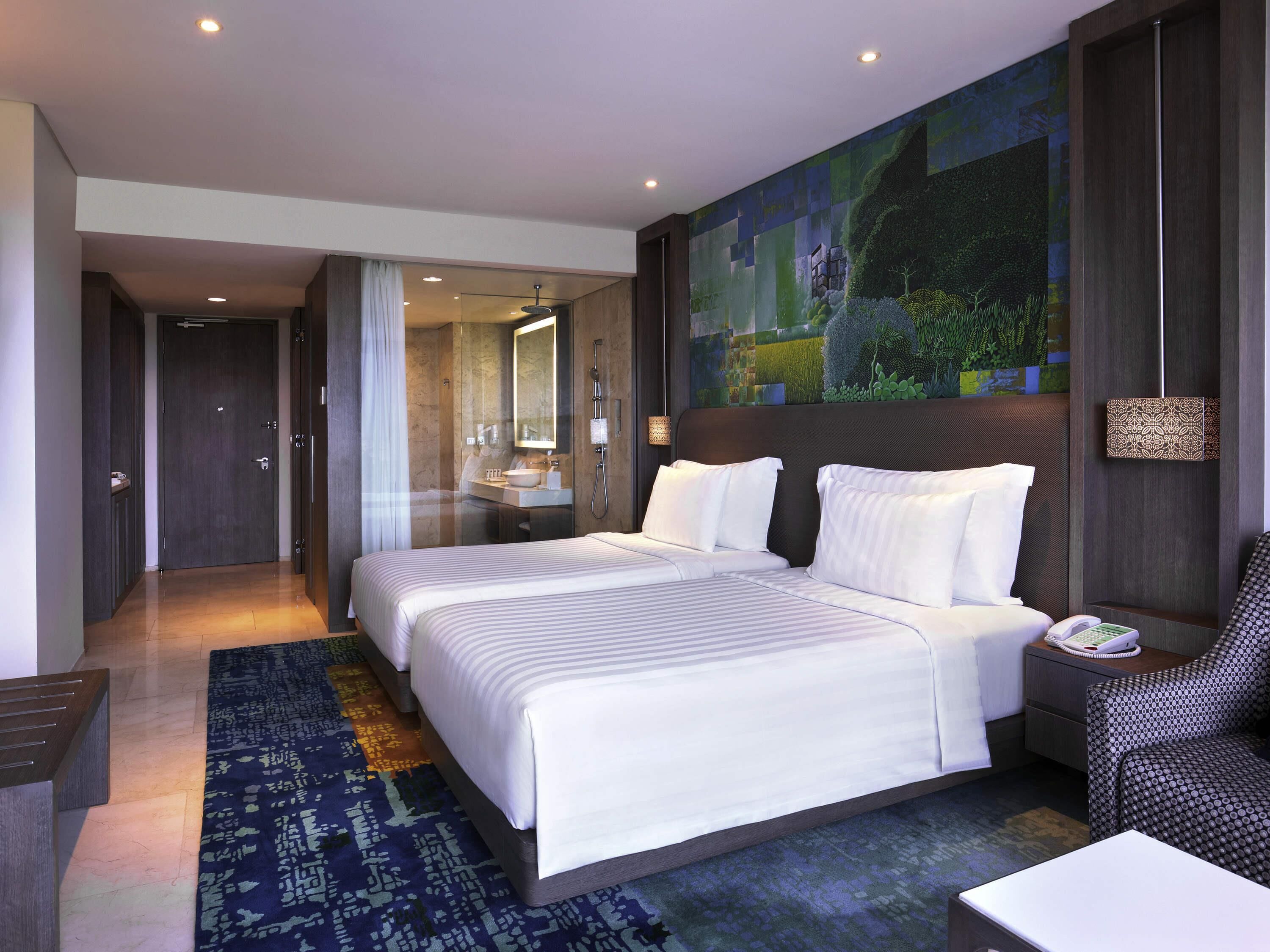 Habitación de hotel con una cama grande, un baño con espejo, una mesita de noche y un teléfono instalado en la pared.