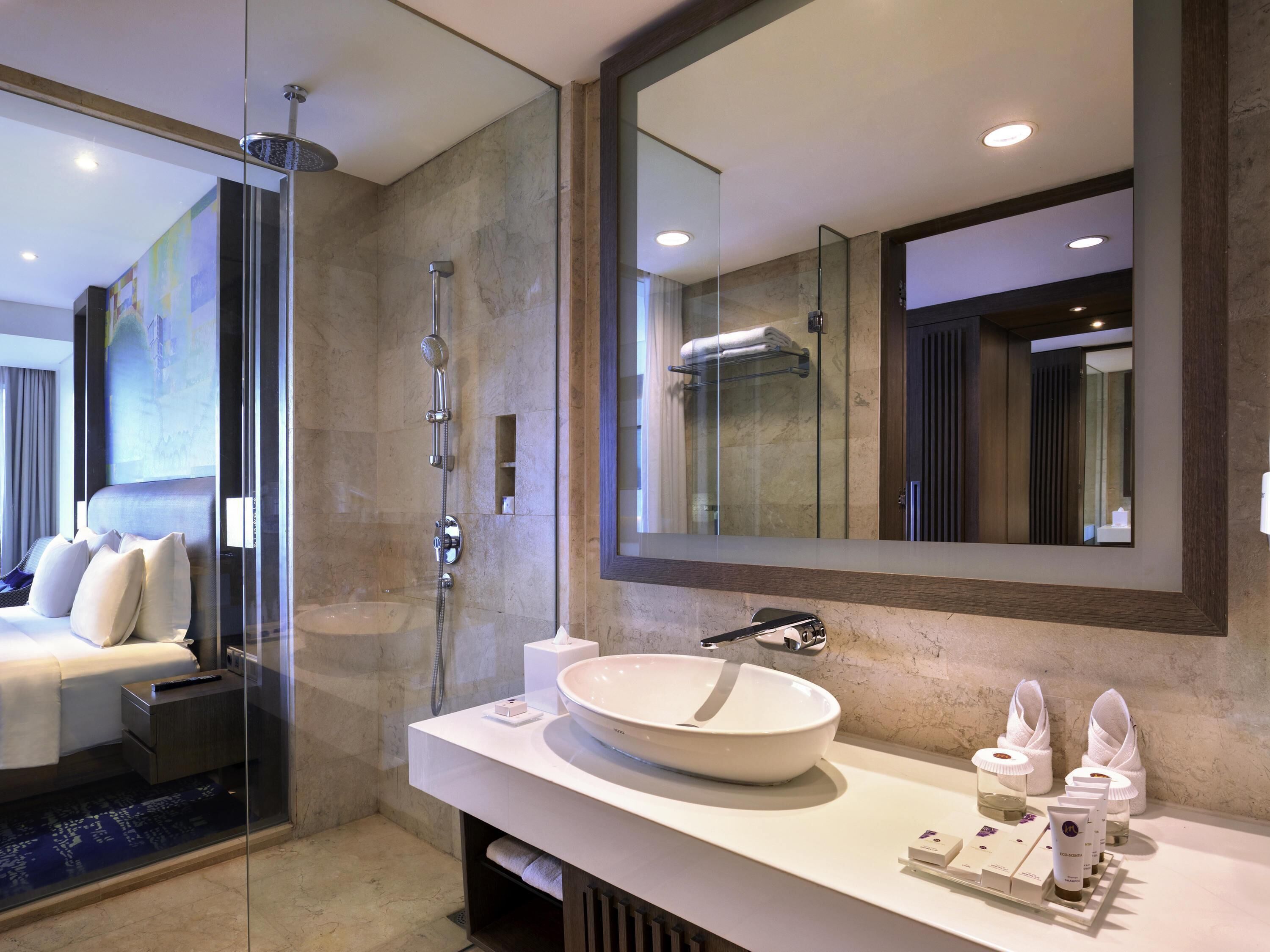 Un baño moderno con cabina de ducha de vidrio, un espejo grande, un lavamanos blanco y artículos de tocador.