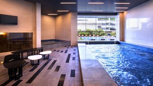 A modern indoor pool area with a seating area and a view of the outside. - Grand Mercure Jakarta Kemayoran (Jakarta)