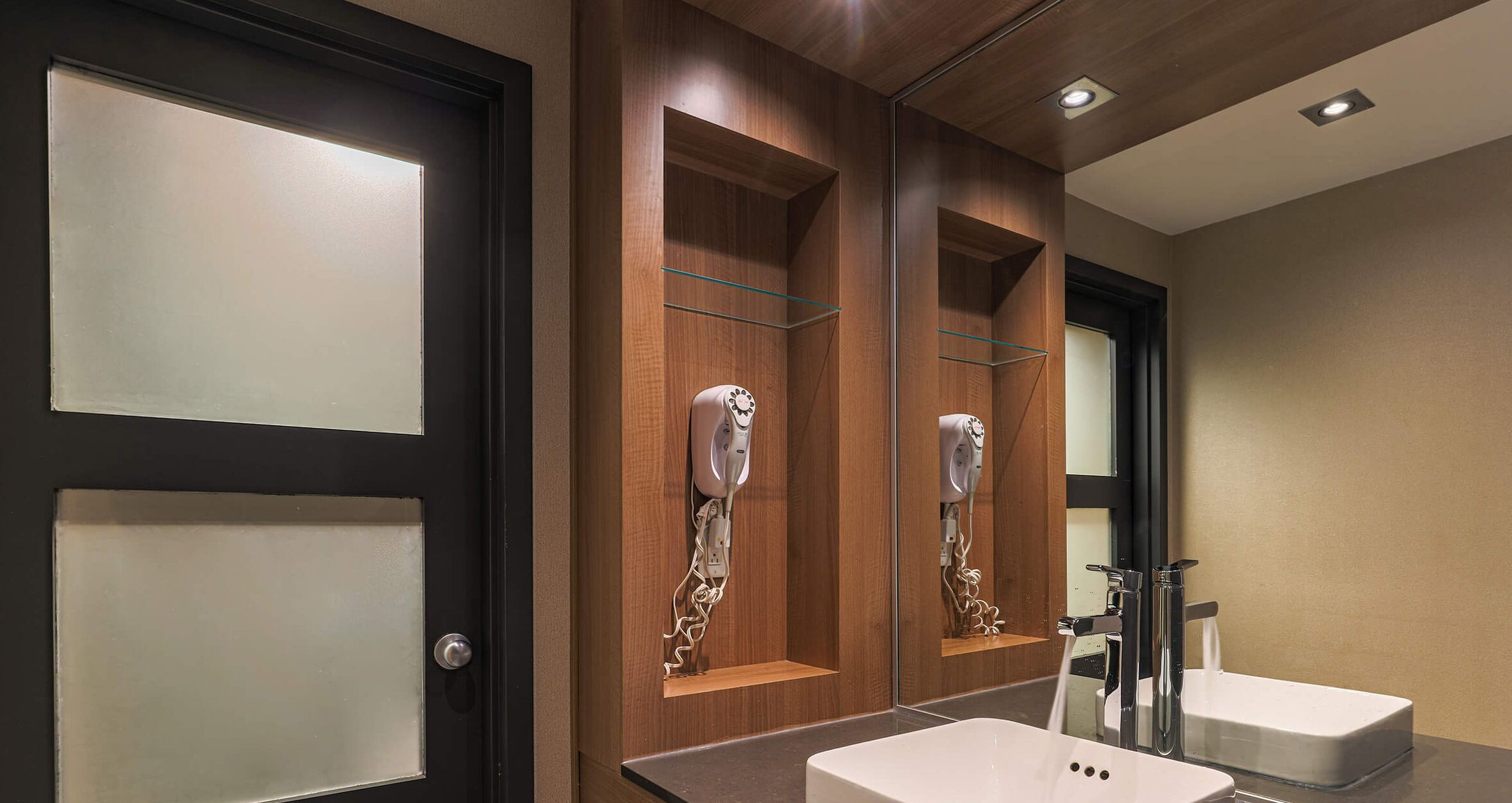 A modern bathroom with a large mirror, a white sink, and a hairdryer mounted on the wall.