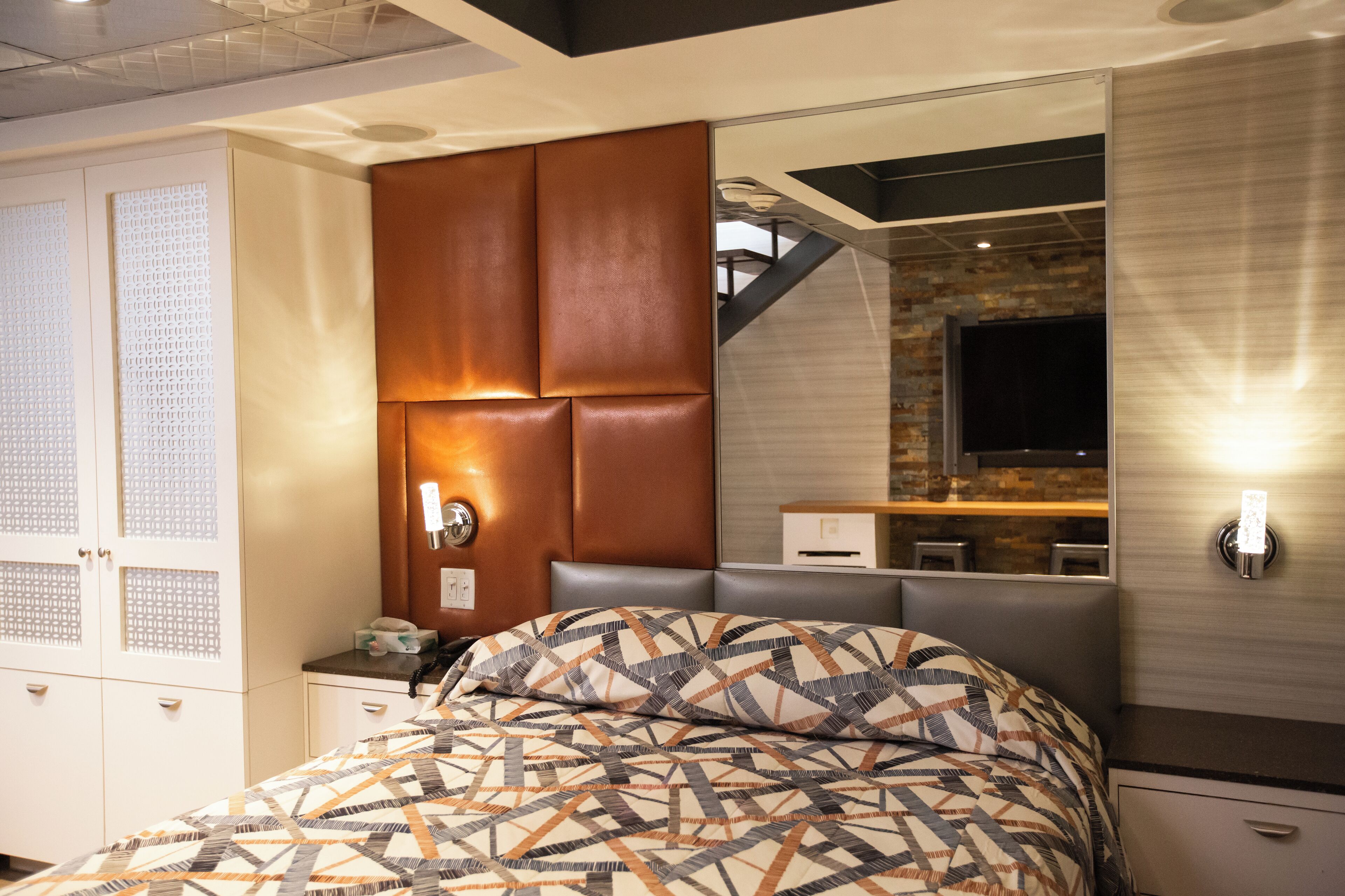 A modern bedroom with a large bed, a built-in headboard, a mirror, and a small desk with a lamp.