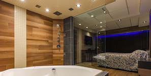 A modern bathroom with a bathtub, wooden wall panels, a glass shower enclosure, and a bed with a patterned cover. - Hôtel Le Chablis (Montreal)