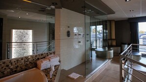 A modern bathroom with a glass-enclosed shower, a marble-tiled vanity, and a seating area with towels. - Hôtel Le Chablis (Montreal)