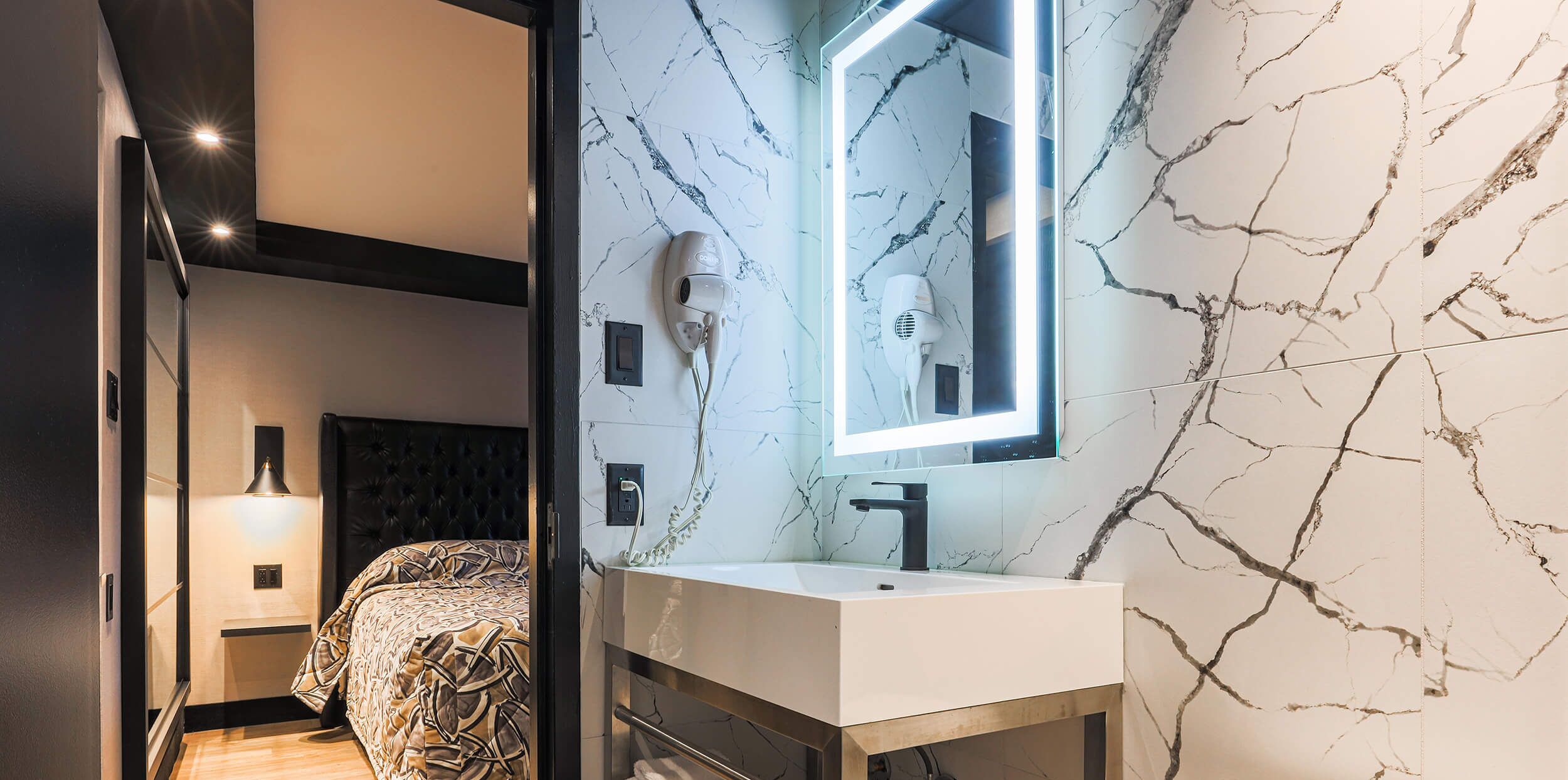 Un baño moderno con salpicadero de mármol, un espejo grande, un secador de pelo y una mesita de noche.