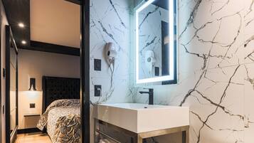 Un baño moderno con salpicadero de mármol, un espejo grande, un secador de pelo y una mesita de noche.