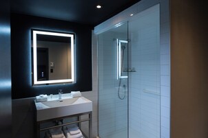 Une salle de bain moderne avec un grand miroir, un lavabo blanc et une douche à parois de verre.