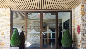 A hotel entrance with stone walls, a wooden ceiling, and a glass door with geometric designs. - Hôtel Le Chablis (Montreal)