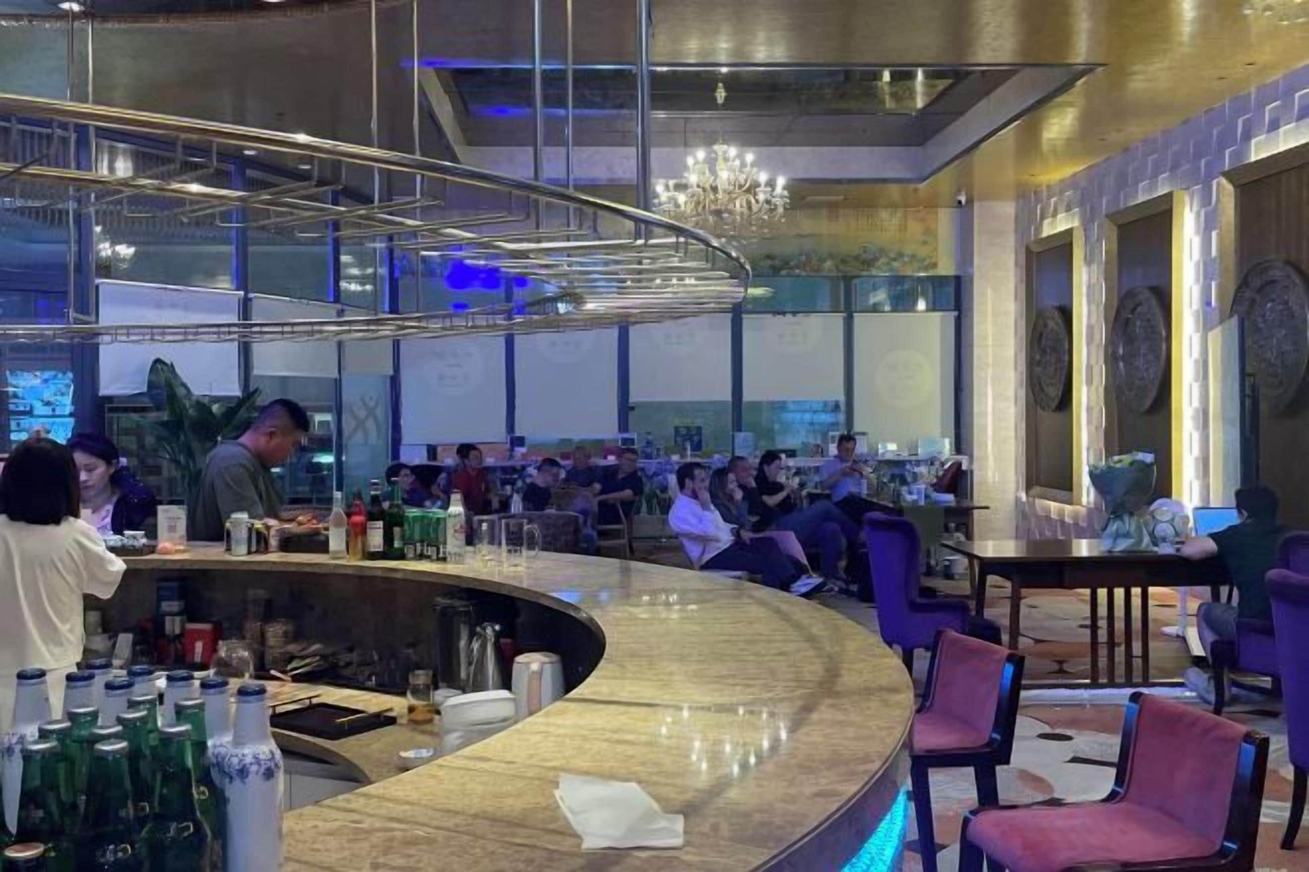 A bar area with a curved counter, seating, and a chandelier.