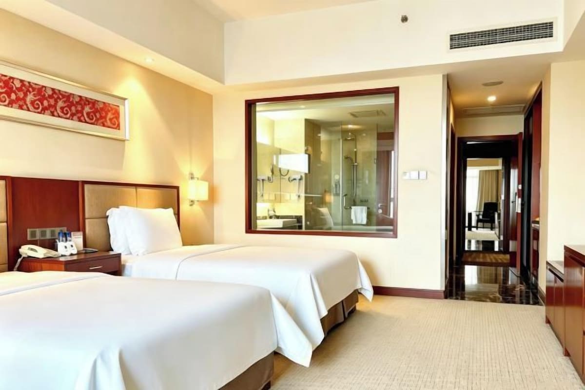A hotel room with two beds, a large mirror, a nightstand, and a bathroom visible through an open door.