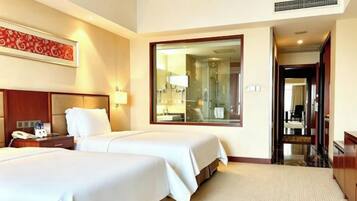 A hotel room with two beds, a large mirror, a nightstand, and a bathroom visible through an open door.