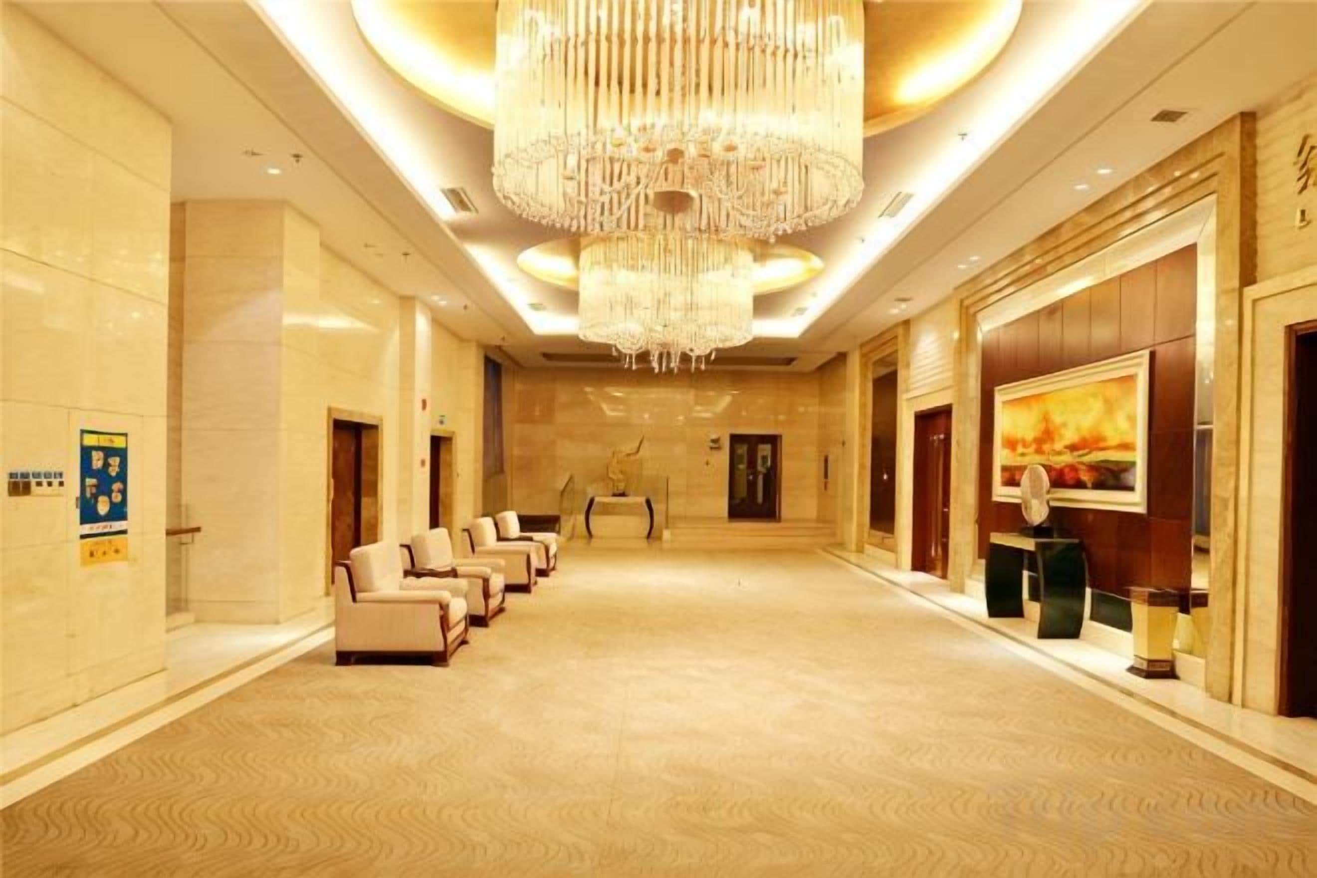 A hotel lobby with a row of seating, a large chandelier, and a reception desk.