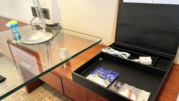 A hotel room with a glass desk, a black storage drawer, a water bottle, a remote control, and a book.
