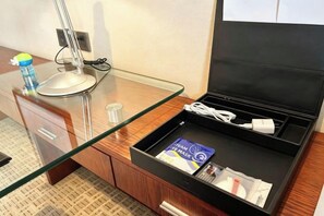 A hotel room with a glass desk, a black storage drawer, a water bottle, a remote control, and a book. - GRAND METROPARK GAOMI (Weifang)