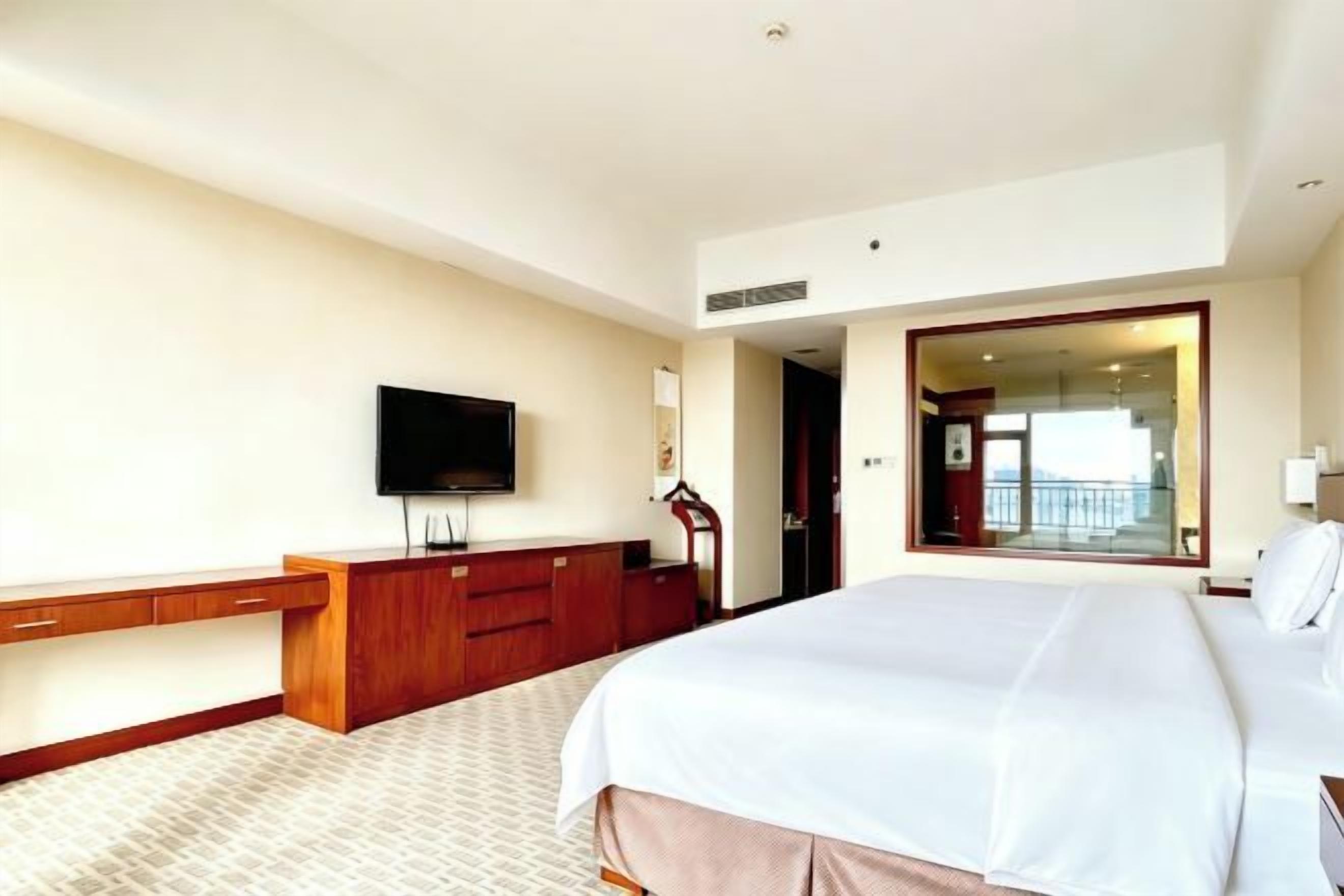 A hotel room with a large bed, a TV, a desk, and a view of the outside.