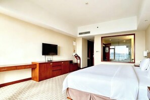 Ein Hotelzimmer mit einem großen Bett, einem Fernseher, einem Schreibtisch und Blick ins Freie.