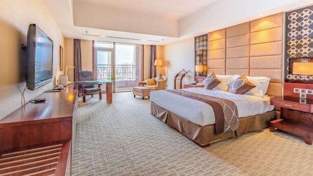 Een hotelkamer met een groot bed, een televisie, een bureau en een balkon.