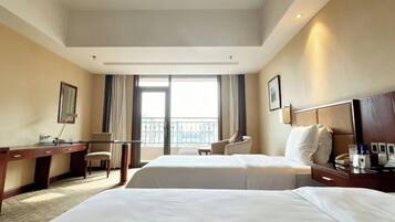 A hotel room with two beds, a desk, a chair, a balcony, and a view of the outdoors.
