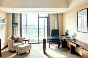 Habitación de hotel con una mesa de vidrio, sofá, escritorio y ventana grande con vistas.