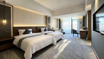 A hotel room with two beds, a desk, and a large window.